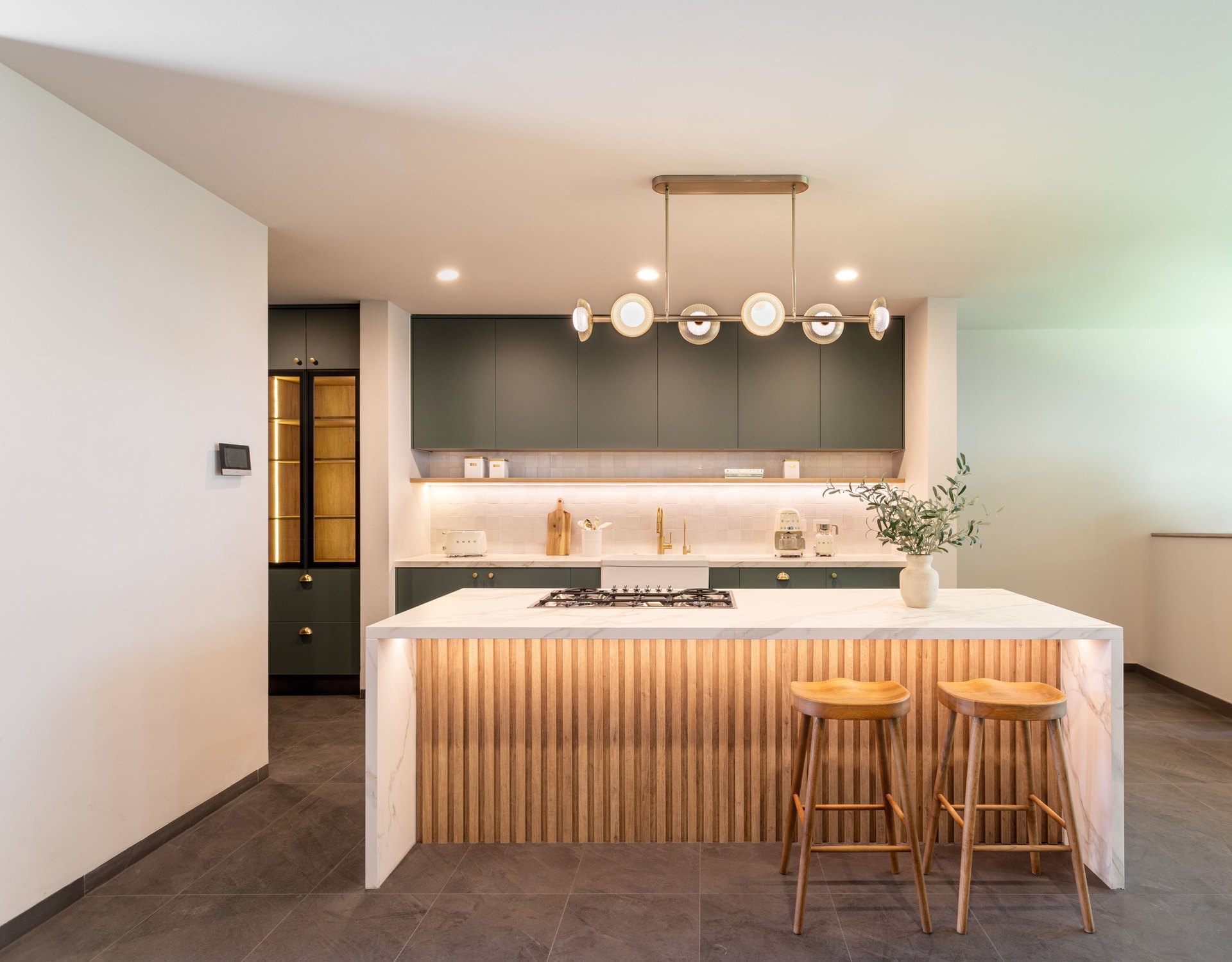 Cocina verde con isla central, cubierta de mármol e iluminación decorativa
